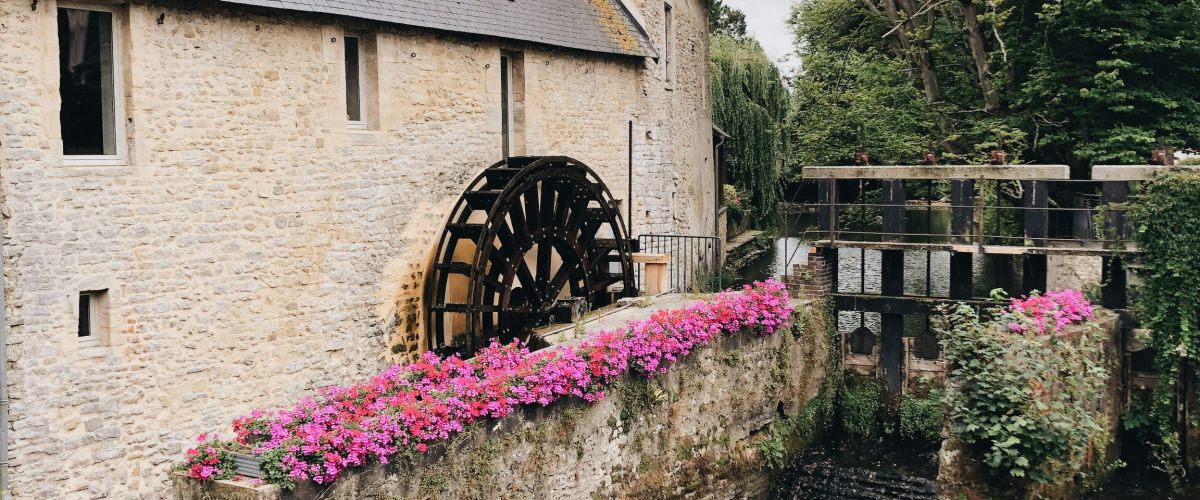 Wassermühle mit Wasserrad, Fluss und Blumenschmuck