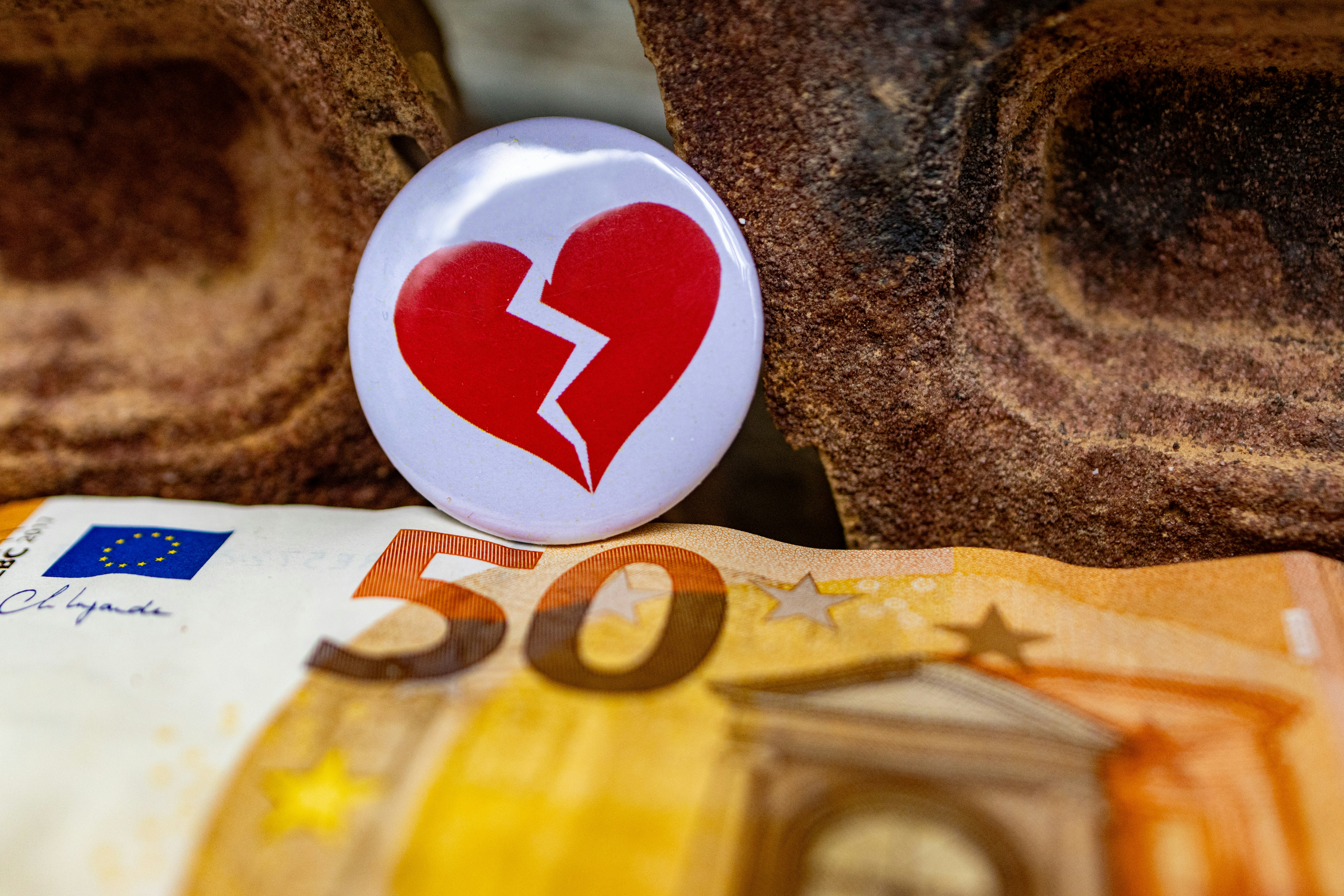 50-Euro-Schein unter einem Ansteckbutton mit zerbrochenem Herzen